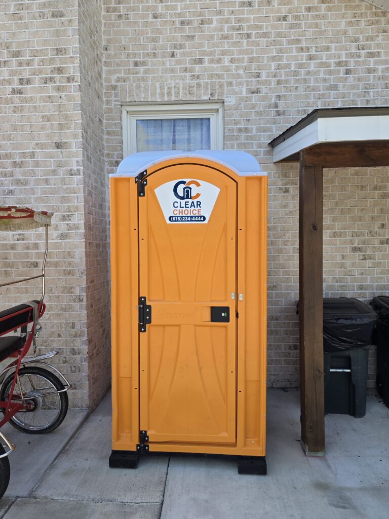 Bright orange portable toilet with Clear Choice Site Services logo placed beside a brick home in Gallatin, TN.